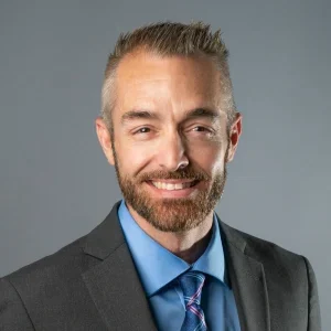 Smiling man in suit with blue shirt.